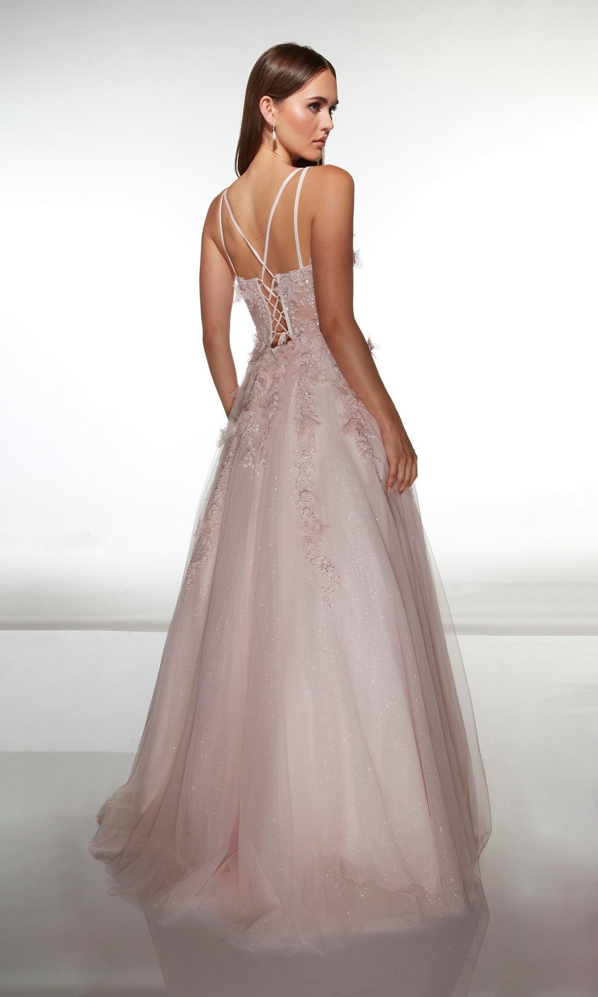 A woman wearing the Alyce 62203 long prom dress in light pink, featuring a corset bodice and lace-up back, stands against a plain white background.